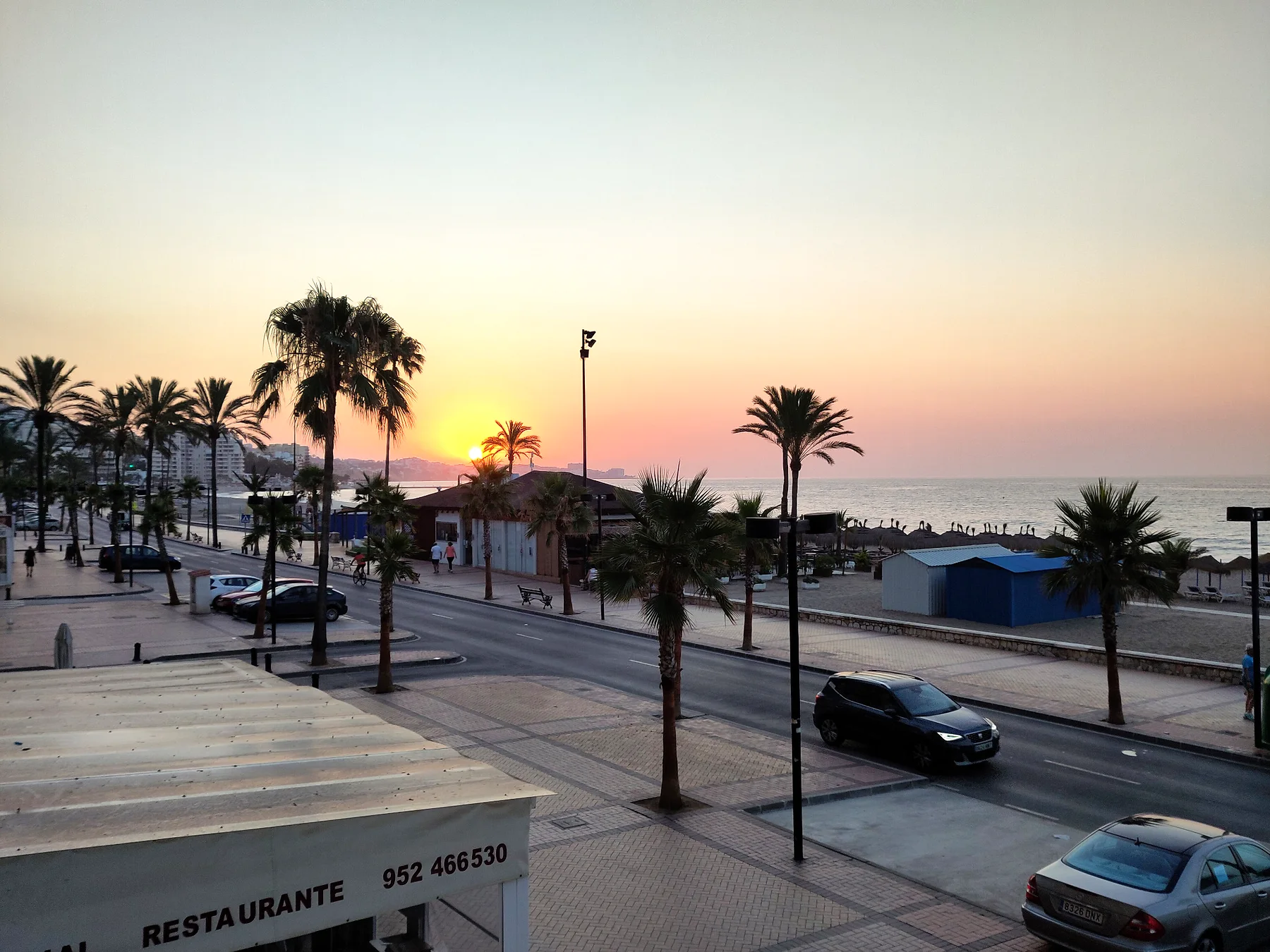 Bredt kig over promenade, palmer og solnedgang i Spanien